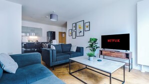 A modern living room with a sofa, coffee table, and a TV displaying 'NETFLIX'. - 3 Bedroom Apartment (Manchester)