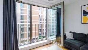 A modern living room with a large sliding glass door leading to a balcony, a dark grey sofa, and a minimalist decor style. - 3 Bedroom Apartment (Manchester)