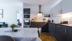 A modern kitchen with dark cabinets, a built-in oven, and a stainless steel range hood. - 3 Bedroom Apartment (Manchester)