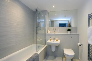 Moderni kylpyhuone, jossa on lasiseinällä varustettu suihku, valkoinen pesuallas ja wc.