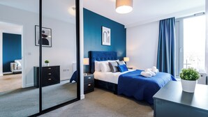A modern hotel room with a large bed, a bedside table, a nightstand, a mirror, and a potted plant.
