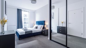 Une chambre moderne avec un grand lit, des tables de chevet, une commode et une porte-fenêtre coulissante donnant sur un balcon.