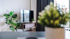Un salon moderne avec un téléviseur à écran plat posé sur un meuble en bois, une plante en pot et une vue sur l’extérieur.