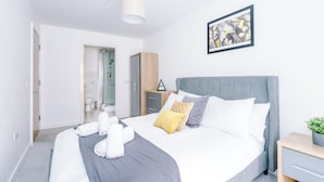 A modern hotel room with a large bed, a bedside table, a nightstand, and a framed artwork on the wall.