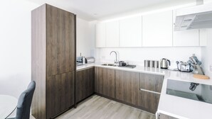 A modern kitchen with dark wood cabinets, white countertops, and stainless steel appliances.