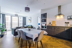 A modern kitchen with stainless steel appliances, a dining area with a table and chairs, and a balcony with a view. - 2 Bedroom Apartment with Balcony (Manchester)