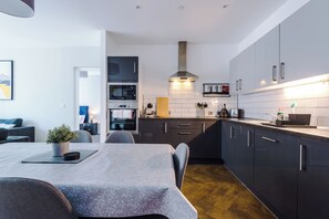 A modern kitchen with dark cabinets, a built-in oven, and a stainless steel range hood. - 2 Bedroom Apartment with Balcony (Manchester)