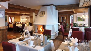 A restaurant with wooden beams, a fireplace, and red chairs. Tables are set with white tablecloths and silverware. - Sporthotel All-Inclusive (Silz)