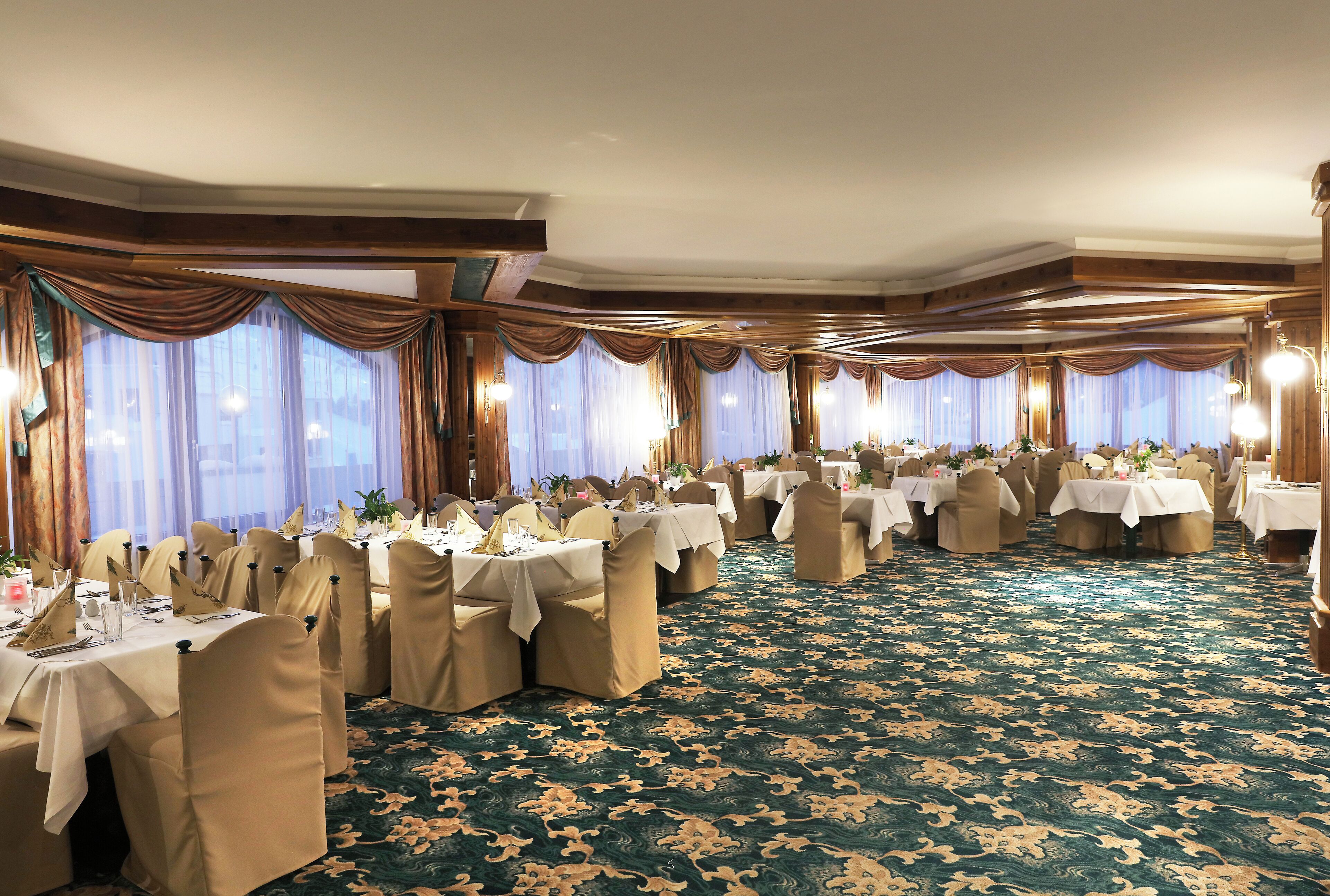 A banquet hall with round tables, beige chairs, and a patterned carpet.