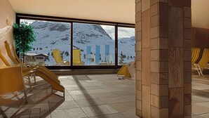 A room with a large window overlooking a snowy mountain. There are yellow chairs and a small table. - Sporthotel All-Inclusive (Silz)