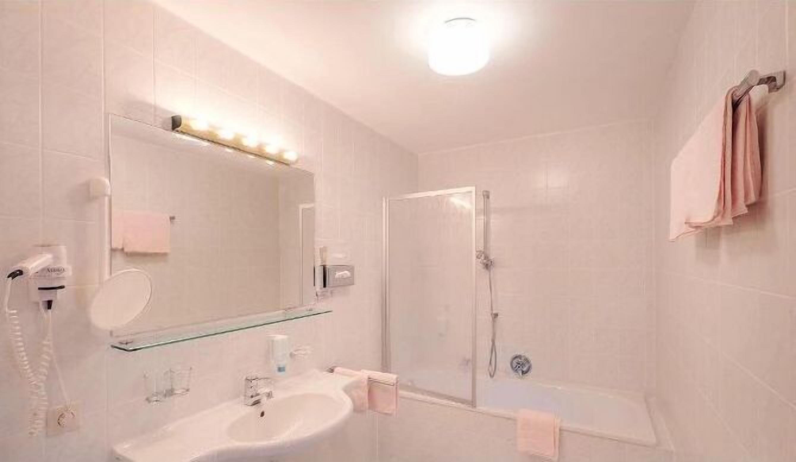 Um banheiro moderno com box de vidro, pia branca e espelho com iluminação acima.