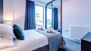 Een hotelkamer met een bed, een groot raam met gordijnen, uitzicht op een gebouw en een radiator aan de muur.
