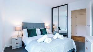 A modern hotel room with a neatly made bed, a large mirror, and a white dresser. - 2 Bedroom Apartment (Manchester)