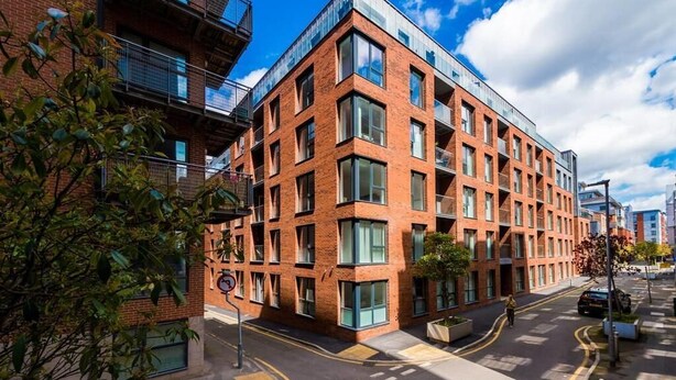 Un edificio moderno in mattoni con ampie finestre e balconi, affacciato su una strada sotto un cielo sereno.