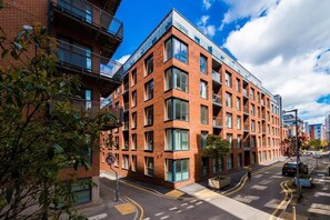 Un bâtiment moderne en briques, doté de grandes fenêtres et de balcons, situé dans une rue où le ciel est dégagé.