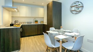 Una cucina moderna con pensili bianchi, un'isola in legno scuro e un'area pranzo con sedie bianche e un tavolo apparecchiato per quattro.
