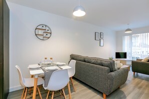 Un salon moderne avec un canapé gris, des chaises blanches et une table à manger dressée pour quatre personnes.