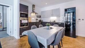 Una cocina moderna con armarios oscuros, electrodomésticos de acero inoxidable y un comedor con mesa y sillas.