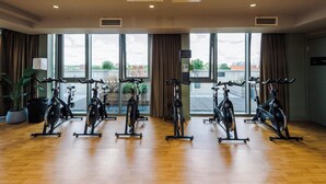 Un gimnasio con bicicletas estáticas dispuestas en filas, ventanas amplias y una planta en maceta.