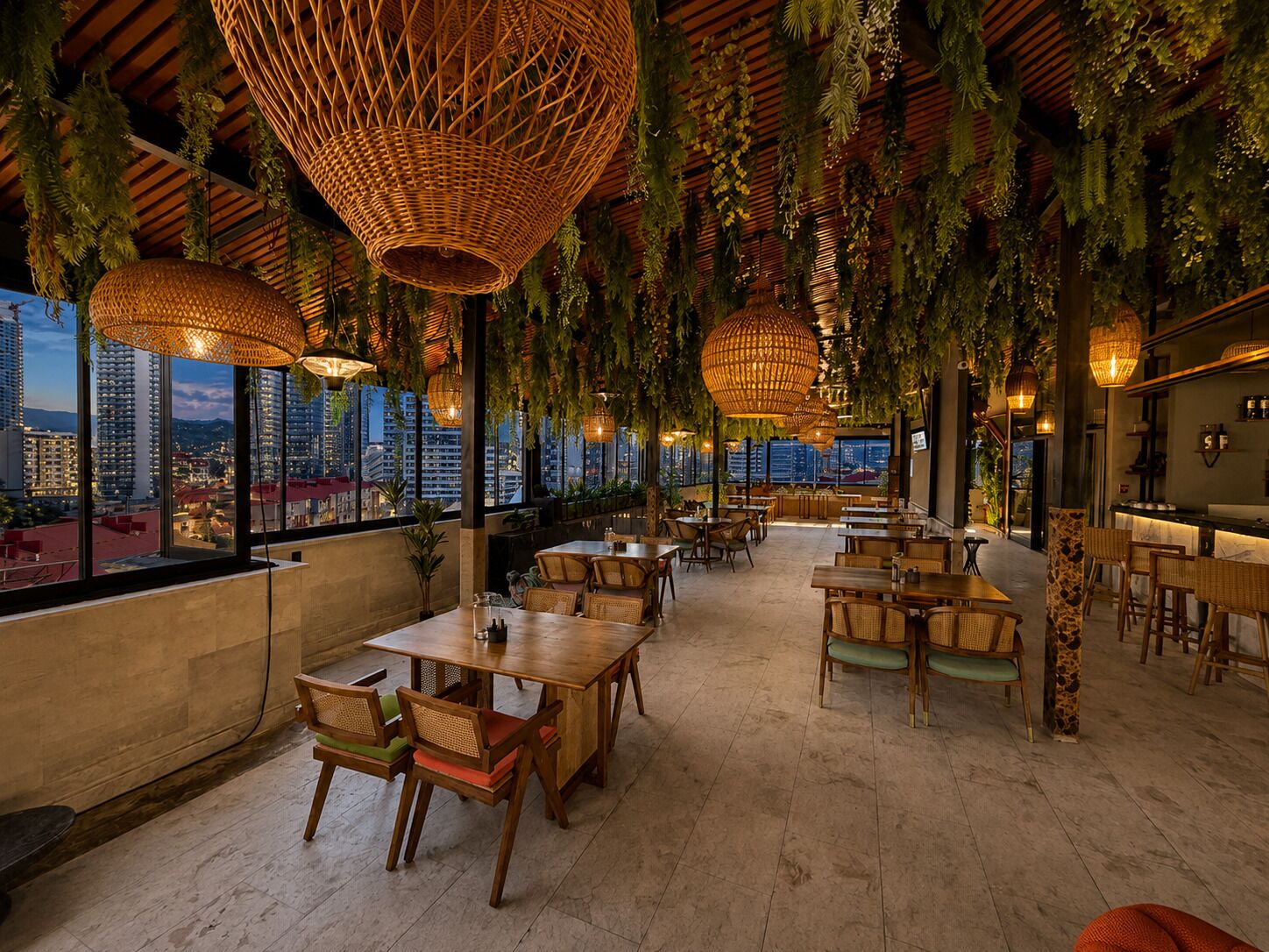 An indoor dining area with tables and chairs, hanging wicker lamps, and a city view through large windows.