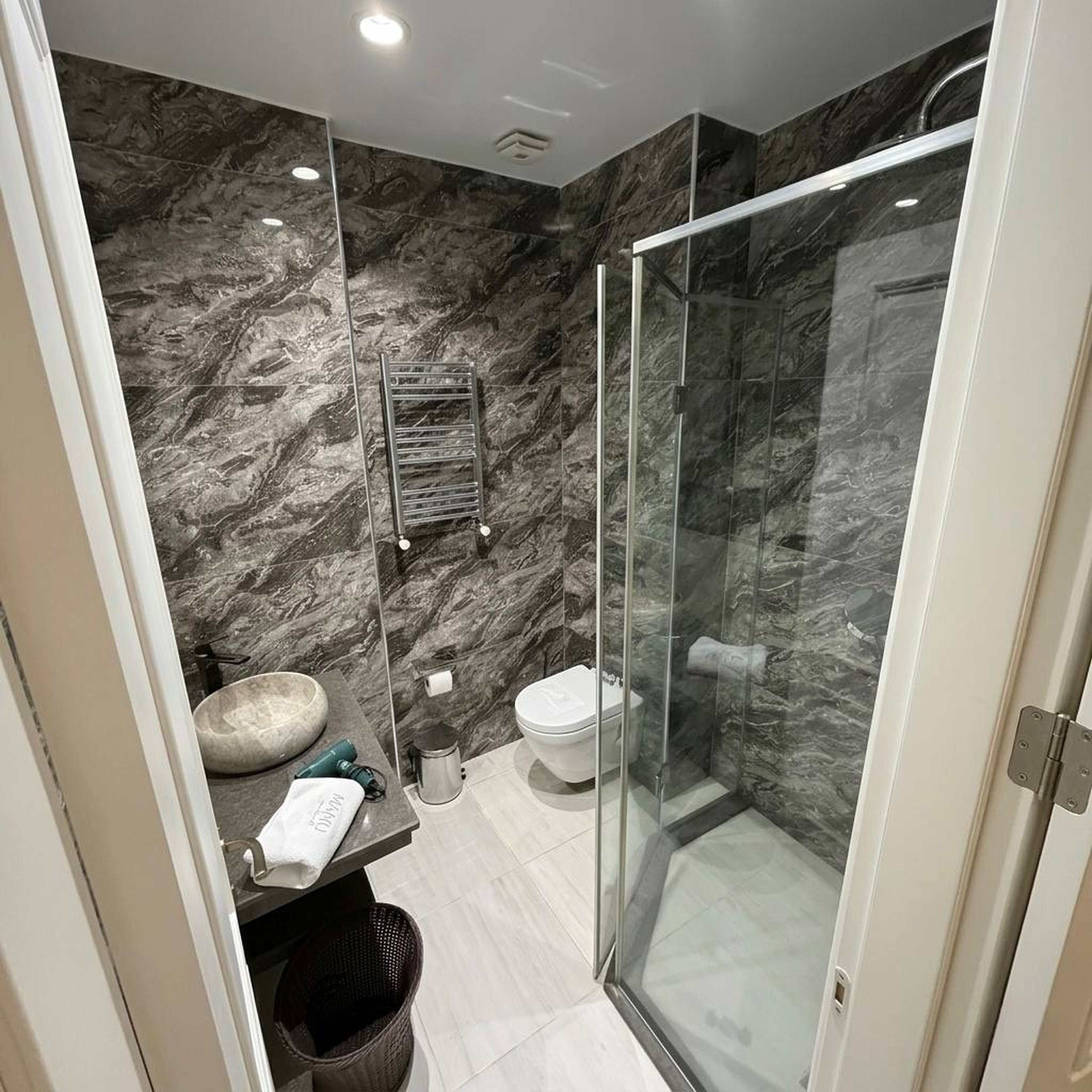 Uma casa de banho moderna com cabine de duche em vidro, parede de mármore e lavatório com toalha.