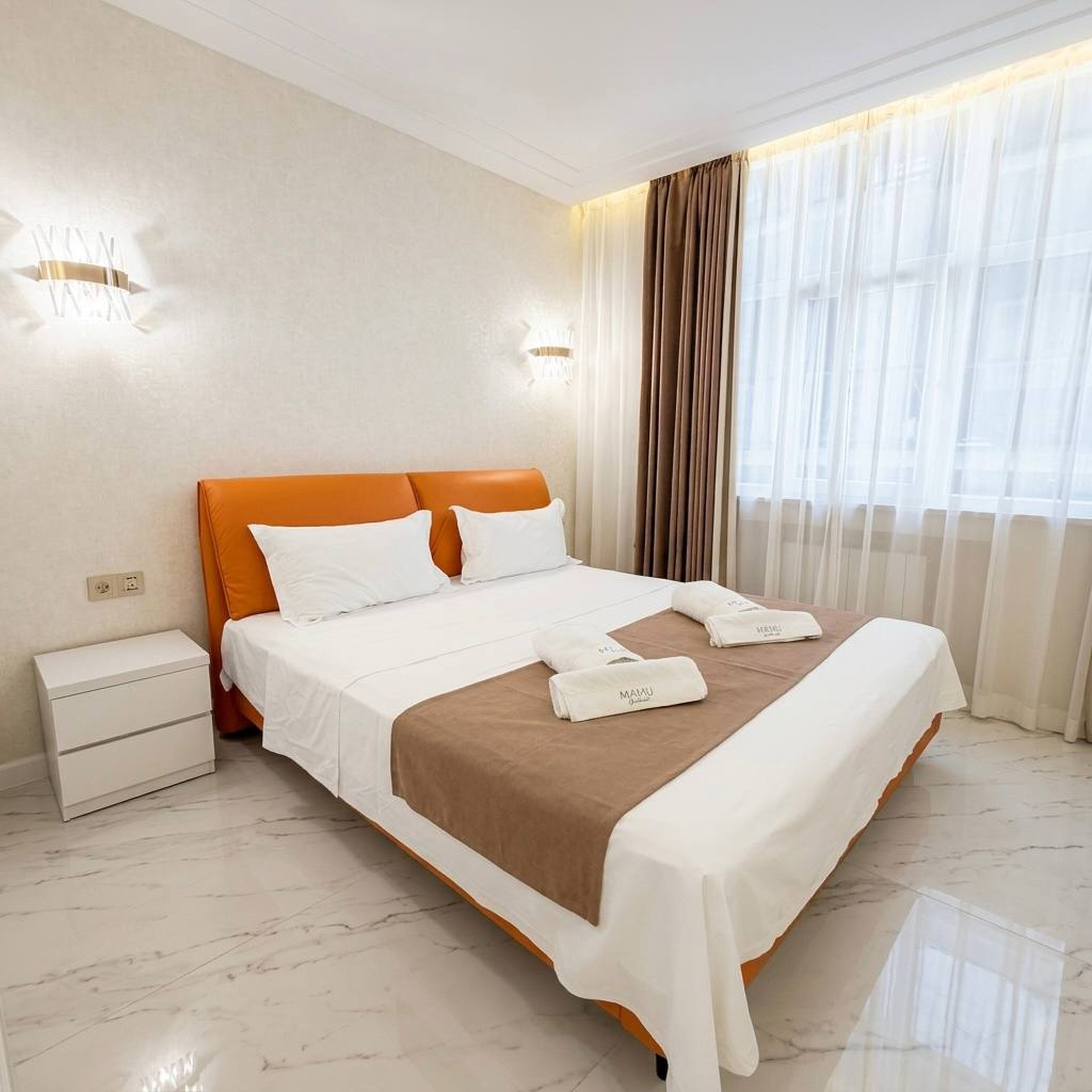 A hotel room with a bed, nightstand, and curtains.