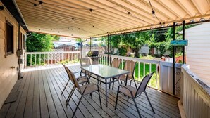 A covered patio with a table and chairs, a grill, and a view of a backyard with a fence and greenery. - Strawberry Peaks Ogden 6 guests (Ogden)