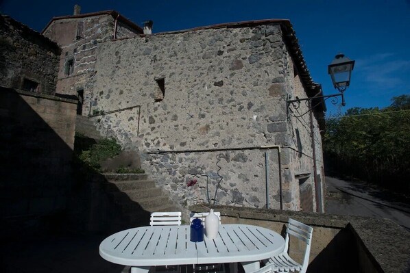 A stone building with a rustic exterior, a round table with chairs, and a street lamp.