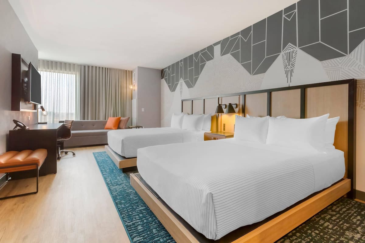 Ein Hotelzimmer mit zwei Betten, einem Schreibtisch, einem Stuhl, einem Fernseher und einer Wand mit Muster.