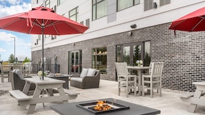 Een terras buiten met vuurkorf, zitplaatsen en rode parasols.