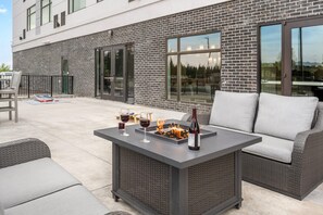 Ein moderner Außenbereich mit Terrasse, einem integrierten Feuerraum, Sitzgelegenheiten und einer Weinflasche.