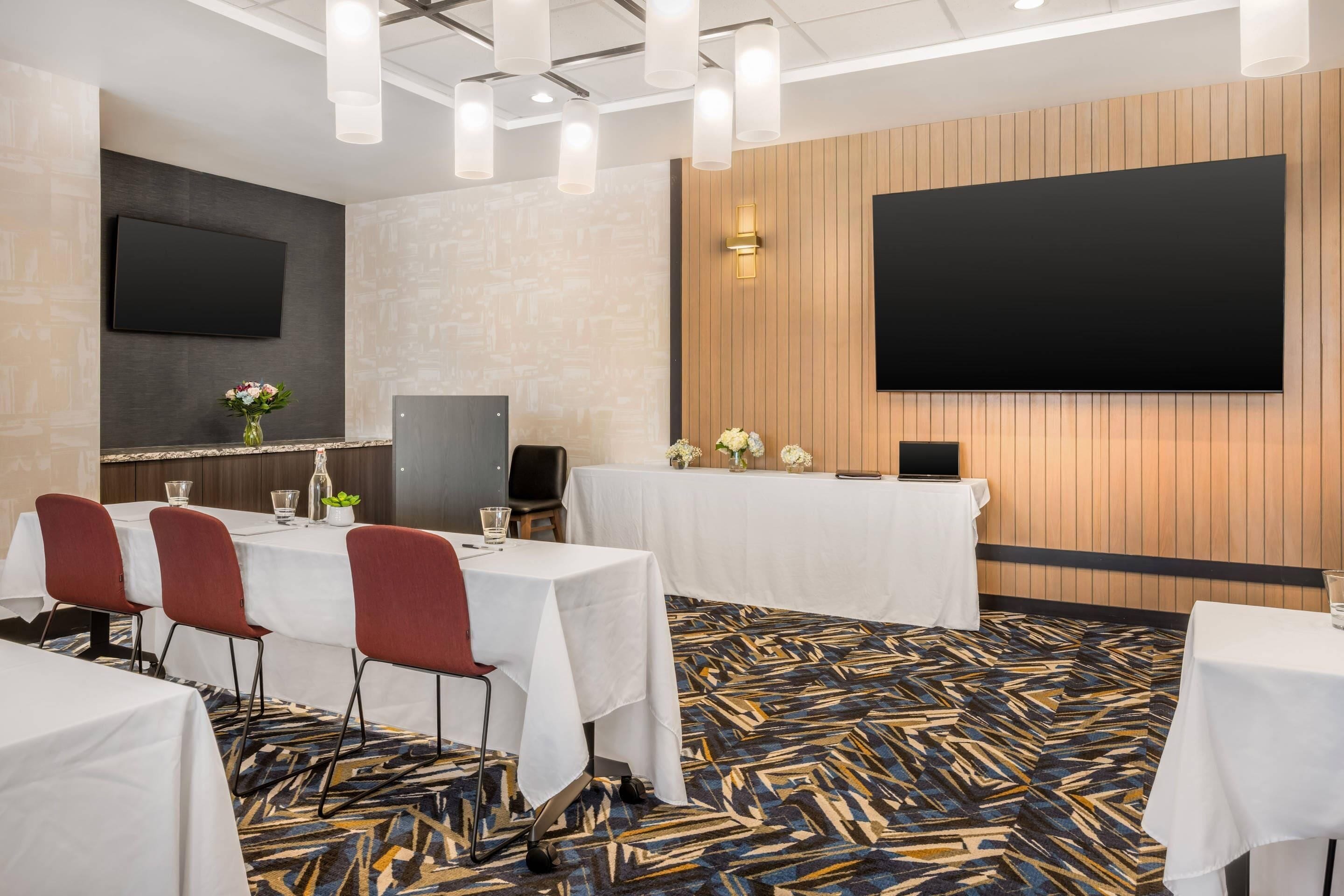 Un salón de conferencias con mesas, sillas, una pantalla grande y una alfombra estampada.
