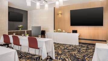 Un salón de conferencias con mesas, sillas, una pantalla grande y una alfombra estampada.