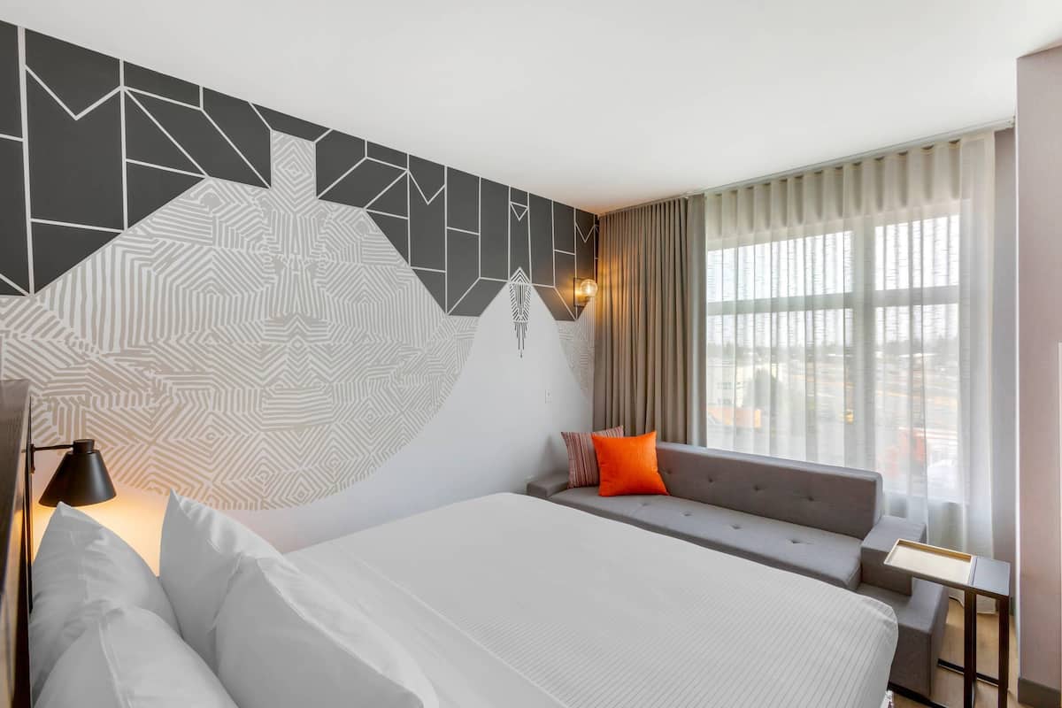 Ein Hotelzimmer mit einem großen Bett, einer Schlafcouch, einem kleinen Tisch und einer Wand mit geometrischen Mustern.