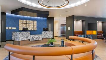 A modern lobby with a reception desk, seating area, and a large screen.