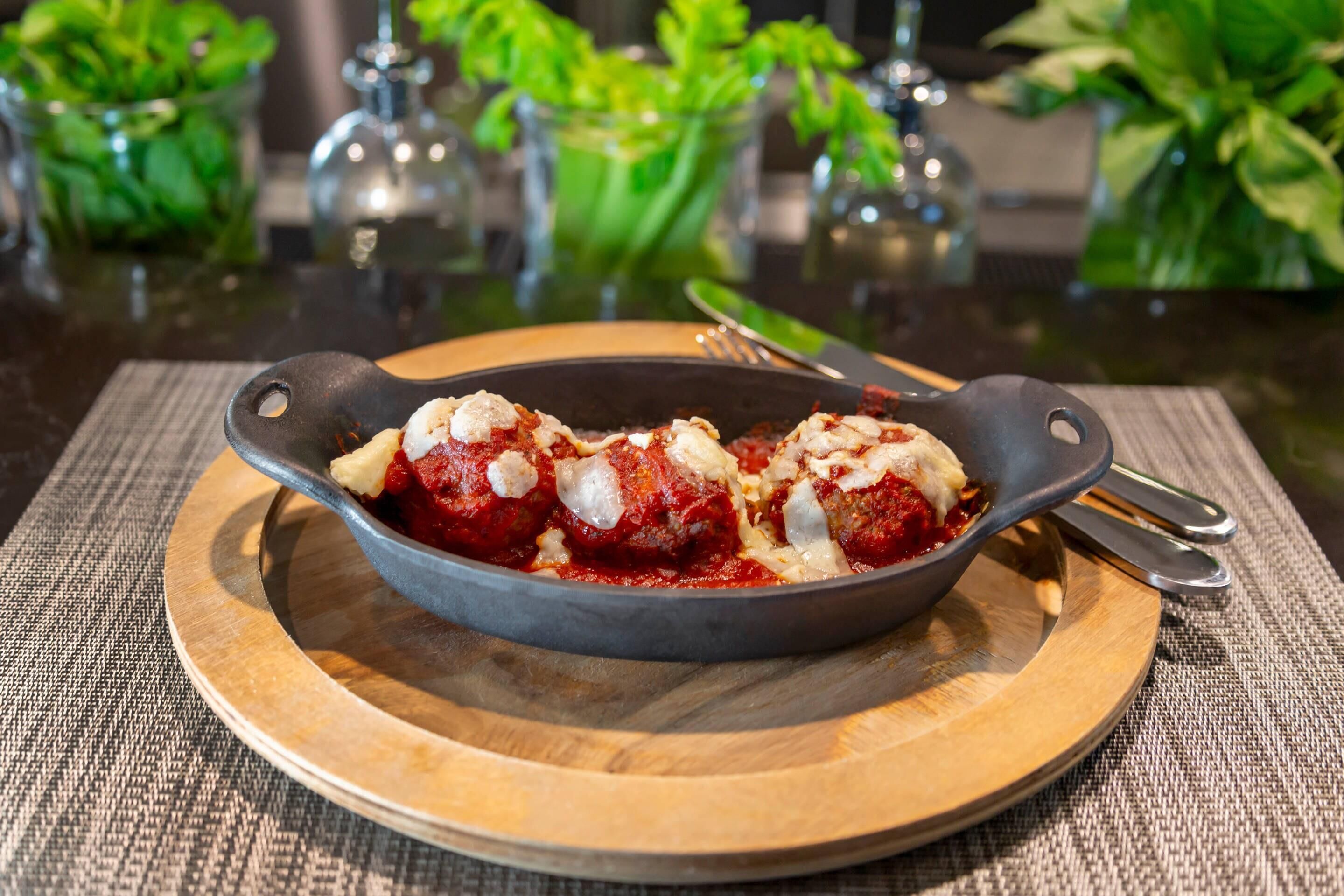 A skillet with meatballs on a wooden board.