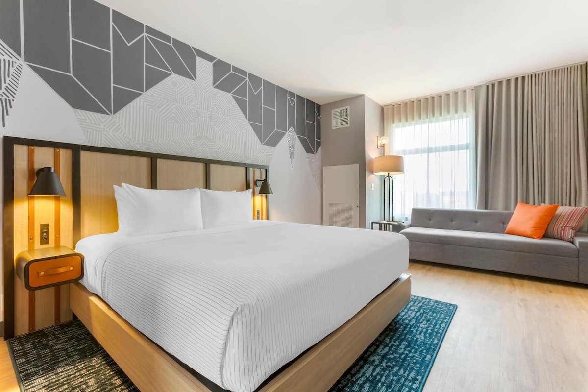 Ein modernes Hotelzimmer mit einem großen Bett, einer Couch und einem gemusterten Teppich.