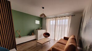 A modern living room with a wooden floor, a brown sofa, a white cabinet, and a green accent wall. - L'alambic à Martial (Menétru-le-Vignoble)
