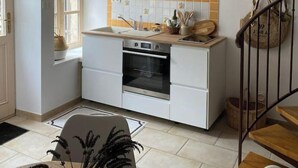 A modern kitchen with white cabinets, a built-in oven, a window, and a hanging light fixture. - L'alambic à Martial (Menétru-le-Vignoble)