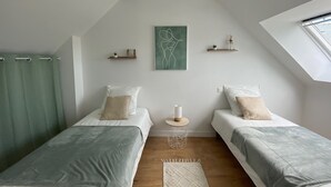 Ein modernes Schlafzimmer mit zwei Einzelbetten, einem Oberlicht, einem abstrakten grünen Gemälde und einem kleinen Nachttisch mit Lampe.