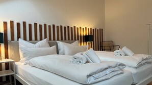 Een net opgemaakt bed met witte lakens en handdoeken, een nachtkastje met een lamp, en een wand met verticale houten latten.