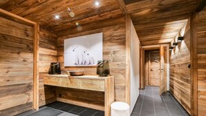 Interior de una cabaña de madera con un banco de madera, un bote de basura blanco y un cuadro de perros en la pared.
