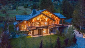 Una cabaña de troncos grande y moderna con un balcón destacado, rodeada de un paisaje exuberante.