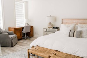 A bedroom with a large bed, a desk, a chair, and a lamp.