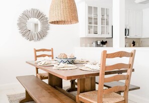A dining area with a wooden table, two chairs, a woven pendant light, and a decorative mirror on the wall.