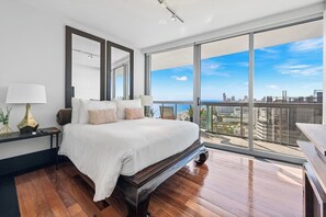 A modern bedroom with a large bed, a nightstand, a lamp, and a view of the city through large windows.