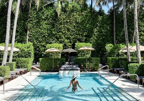 Ein Swimmingpool mit Liegestühlen und Sonnenschirmen, umgeben von Grünflächen und Palmen.
