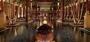 A spacious indoor area with a central water feature, seating areas, and tall columns.