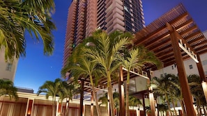 A hotel with tall buildings, palm trees, and a wooden pergola structure.