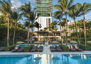 A hotel with a swimming pool, palm trees, and a modern building with balconies.